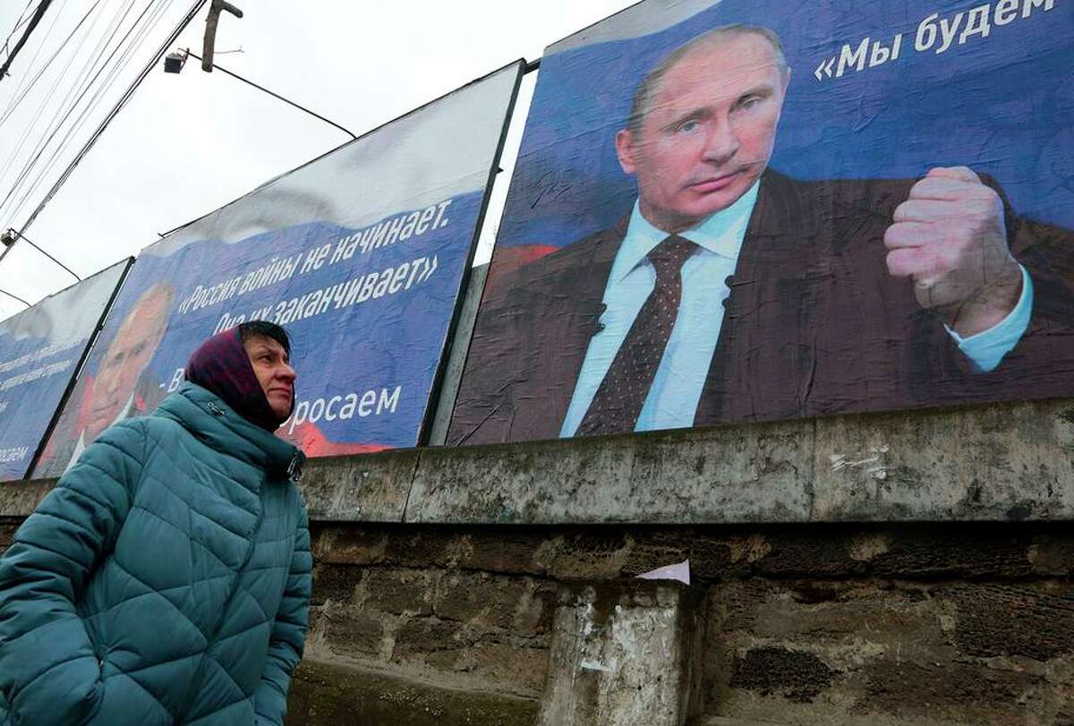 A woman walks past huge placards bearing images of Russian President Vladimir Putin and that read “Russia does not start wars, it ends them” and “We will aim for the demilitarization and denazification of Ukraine” in the city center of Simferopol, Crimea. Russian-sponsored messaging has been rampant online, and social media companies are struggling with how to deal with misinformation.