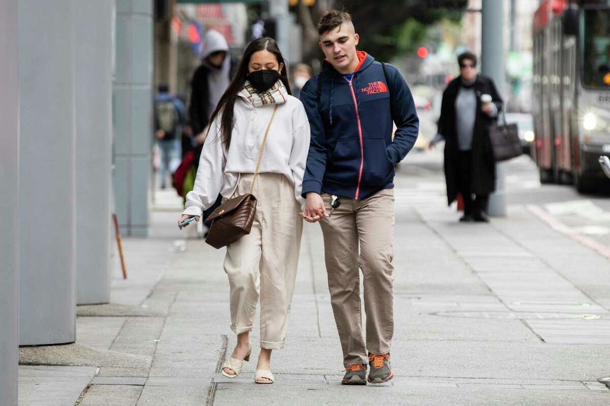 A pedestrian wears a mask while the other goes mask-free as they cross 4th Street at Mission Street in San Francisco. It may be another four to six weeks before coronavirus cases bottom out from their peak a few weeks ago.