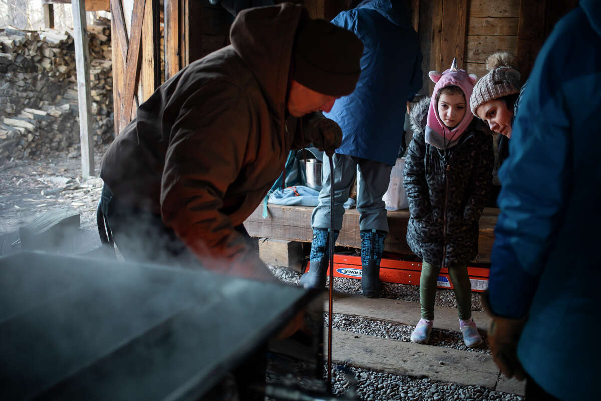 Reagan Douglas, 7, center, and Maria Douglas, right, watch as Philip Meister, left, demonstrates how maple sap is boiled down into syrup inside the sugarhouse during the "Tap a Tree" event Thursday, March 3, 2022 at Chippewa Nature Center in Midland.