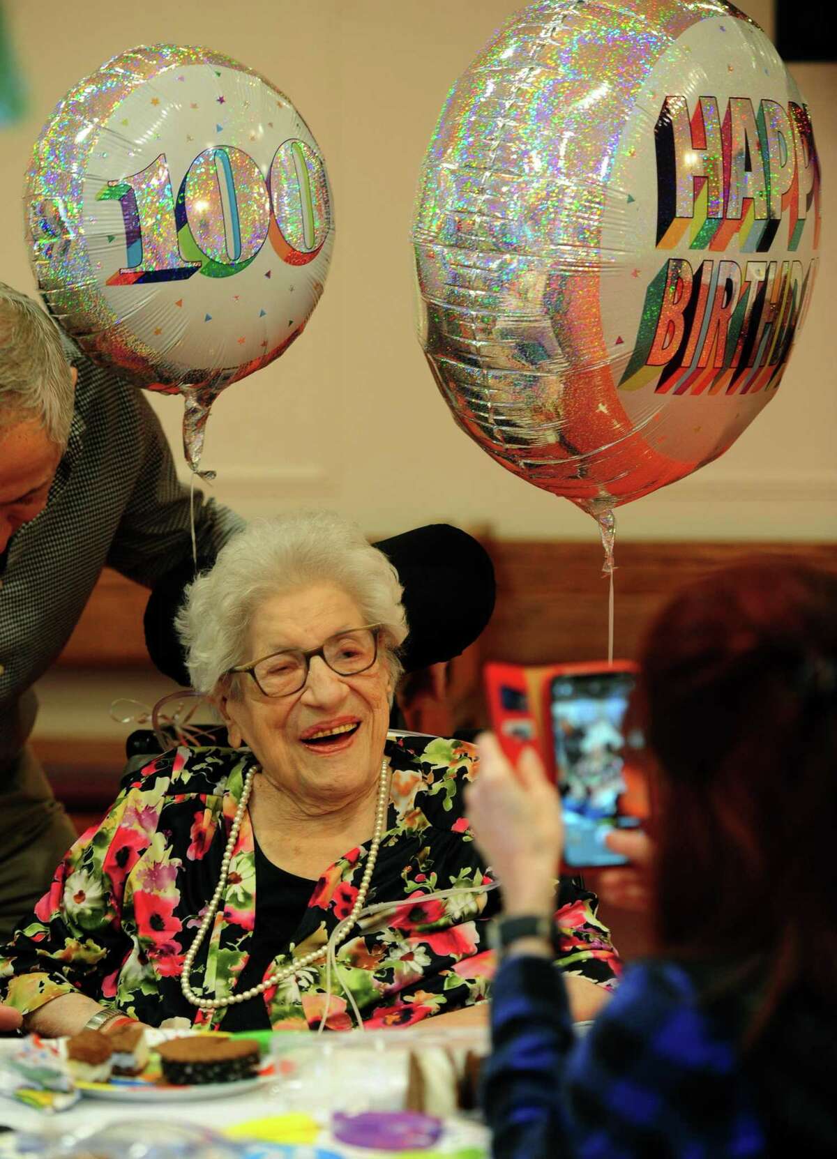 Nathaniel Witherell employee Mary Tate takes a photo of Frances Carino as she celebrates her 100th birthday with her family at the senior care facility in Greenwich, Conn., on Friday March 4, 2022. At left is her son Peter and granddaughter Elizabeth.