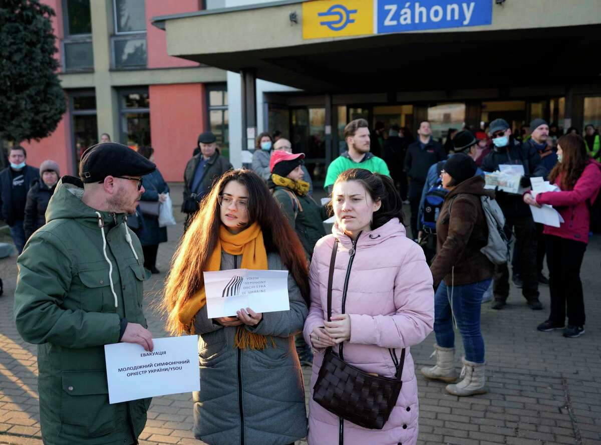 Slovenian volunteer Uros Dokl, left, and violin player Myroslava Sherbina, center, wait for members of the Youth Symphonic Orchestra of Ukraine at the train station in Zahony, Hungary, Sunday, March 6, 2022. When Russia's invasion of Ukraine began and air raid sirens rang out in the embattled region of Donbas, Myroslava Sherbina rushed from her home and into a bomb shelter bringing only two of her possessions: the clothes on her back, and her violin.