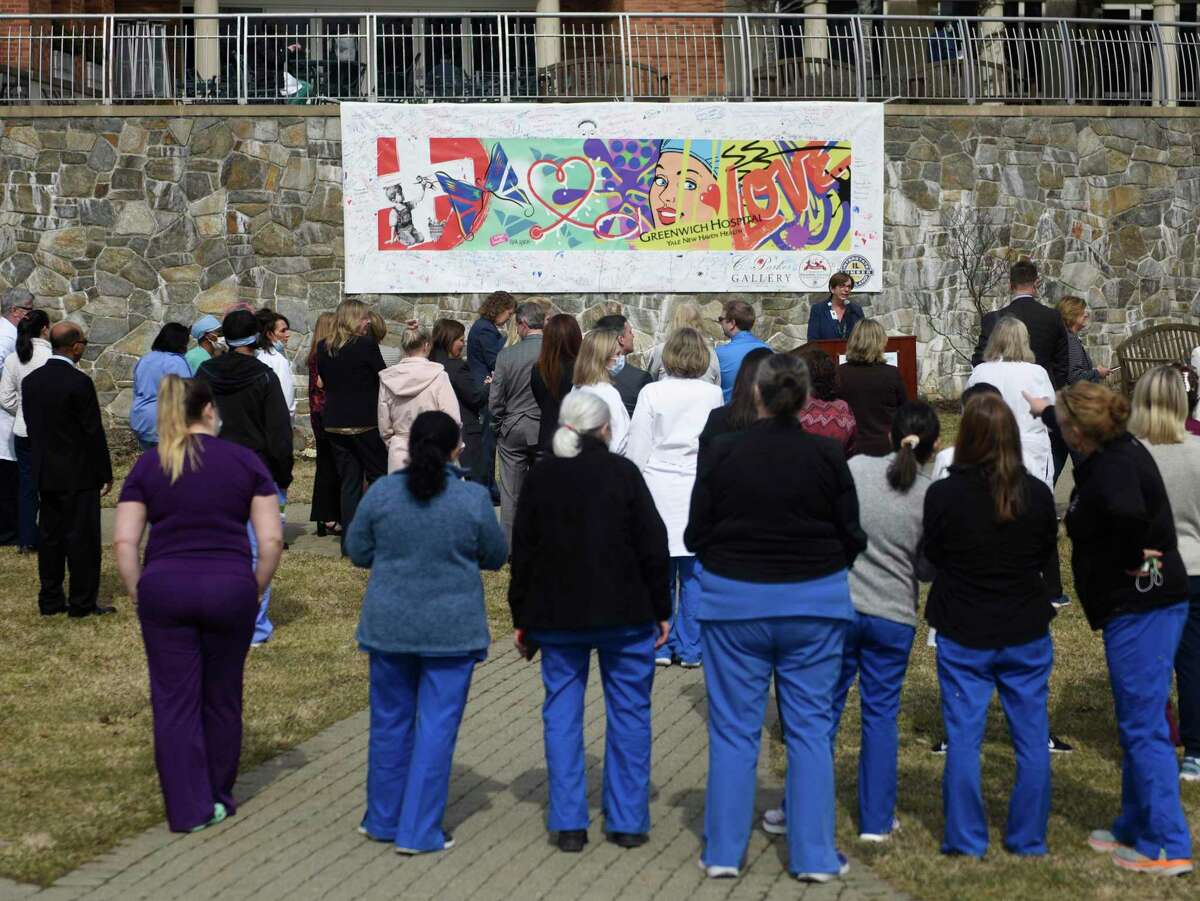 Hospital workers look upon a new banner in the courtyard at Greenwich Hospital in Greenwich, Conn. Monday, March 7, 2022. The hospital unveiled and dedicated a mural by artist Rick Garcia in appreciation of the efforts of hospital workers during the pandemic. Sponsored by Greenwich's C. Parker Galley, the banner was available for attendees of the Greenwich Reindeer Festival at Sam Bridge Nursery and Greenhouses to sign.