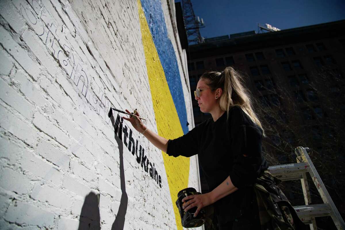 Houston artist Shelbi Nicole paints the words “stand with Ukraine” next to a mural in the shape of a heart and the Ukrainian flag colors, Monday, Feb. 28, 2022, in Houston.