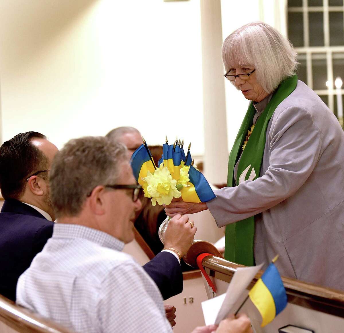 The Rev. Pat Kriss, Pastor of First Congregational Church in Danbury, passes out flowers and a small Ukrainian flag at the start of a peace vigil for Ukraine and the world Monday evening, March 7, 2022.