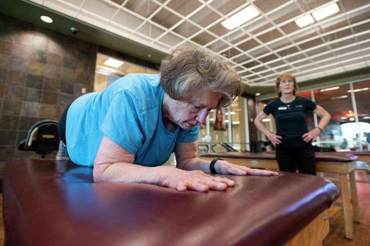 Kevin Tidd does a one minute plank while her trainer Marcia Noyes watches the time in Life Time Monday, Feb. 28, 2022, in Katy, Texas. When Kevin first started working out she could not do a plank because her stomach was in the way.