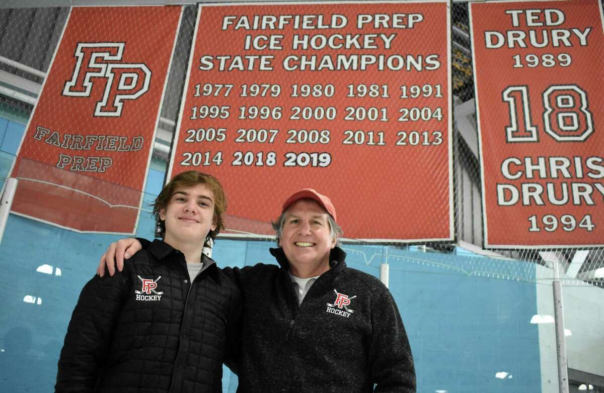 Fairfield Prep senior goalie Tommy Martin poses with his father Kevin Martin, who won three state titles as the Fairfield Prep goalie from 1978-1981, in front of the Fairfield Prep state championship banner at the Wonderland of Ice rink in Bridgeport on Friday, Feb. 19, 2021. (Pete Paguaga, Hearst Connecticut Media)