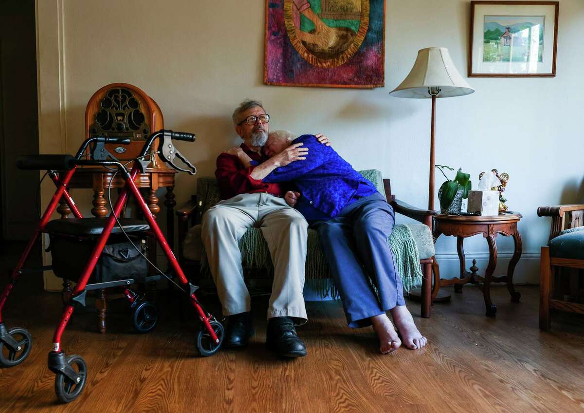 约翰·沙利文和帕特·麦克亨利·沙利文在奥克兰的客厅里拥抱在一起。麦克亨利·沙利文是她丈夫的看护人和痴呆症倡导者，这些责任加上对严重疾病的恐惧限制了她在大流行期间的工作能力。