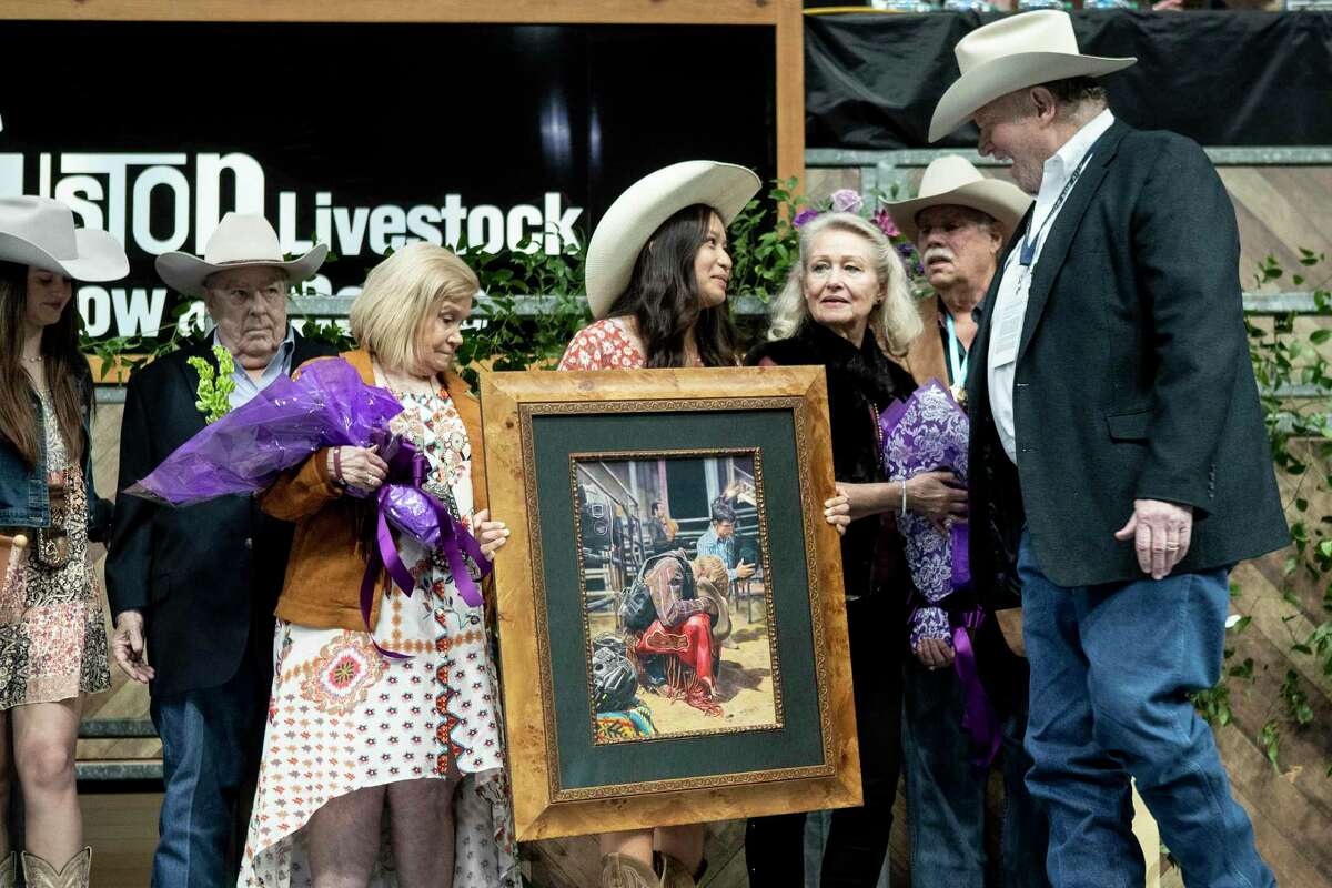 Gracin Nguyen, center, talks to Paul Somerville, as he holds her Grand Champion artwork, a colored drawing titled “In His Hands, was bought during the school art auction at the Houston Livestock Show and Rodeo on Sunday, March 13, 2022 in Houston. Nguyen’s drawing brought a bid of $250,000.