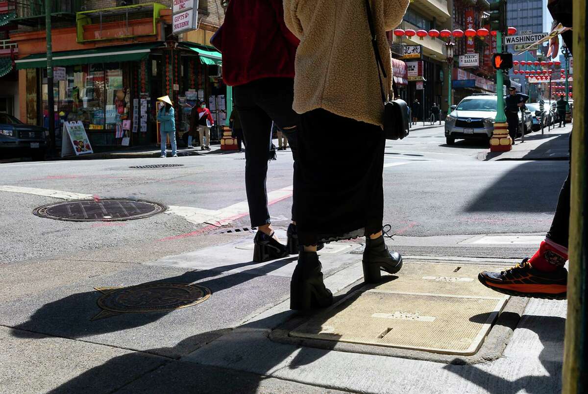 Two women walk toward Washington Street as another woman stands at the opposite corner with a handful of promotional flyers in San Francisco’s Chinatown on March 14, 2022. The Bay Area has been a flashpoint for anti-Asian bias, as well as renewed community activism to combat it.