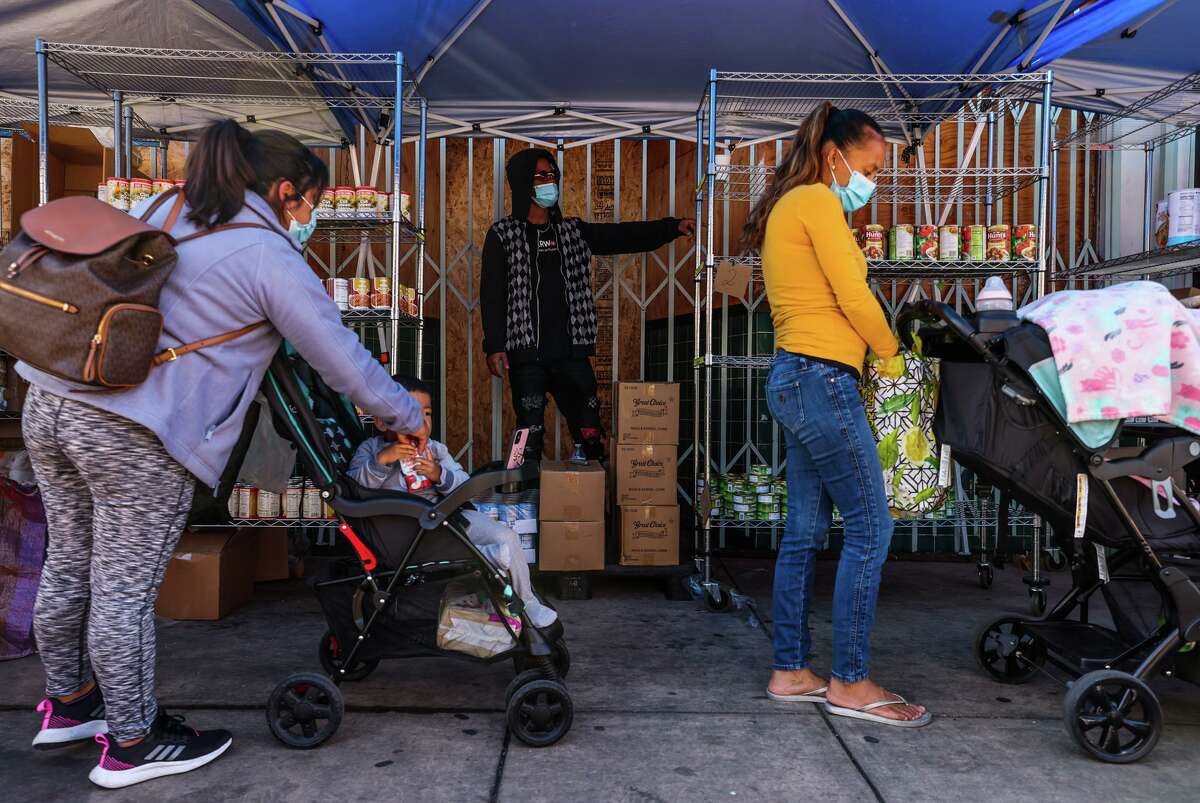 Gregory Stone (center) stands between shelves of canned goods while working the food line at Homies Empowerment’s “Freedom Store.” in Oakland.