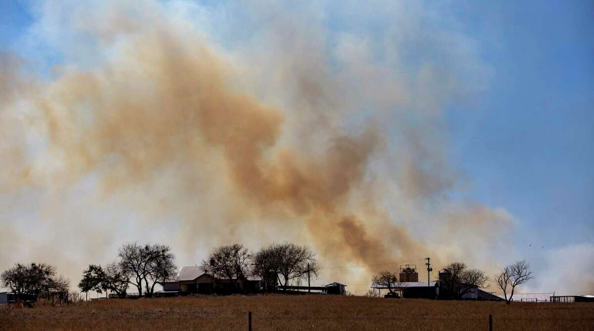 Smoke from a wildfire rises Tuesday, March 15, 2022, behind homes on the Peeler Ranch south of Jourdanton in Atascosa County.