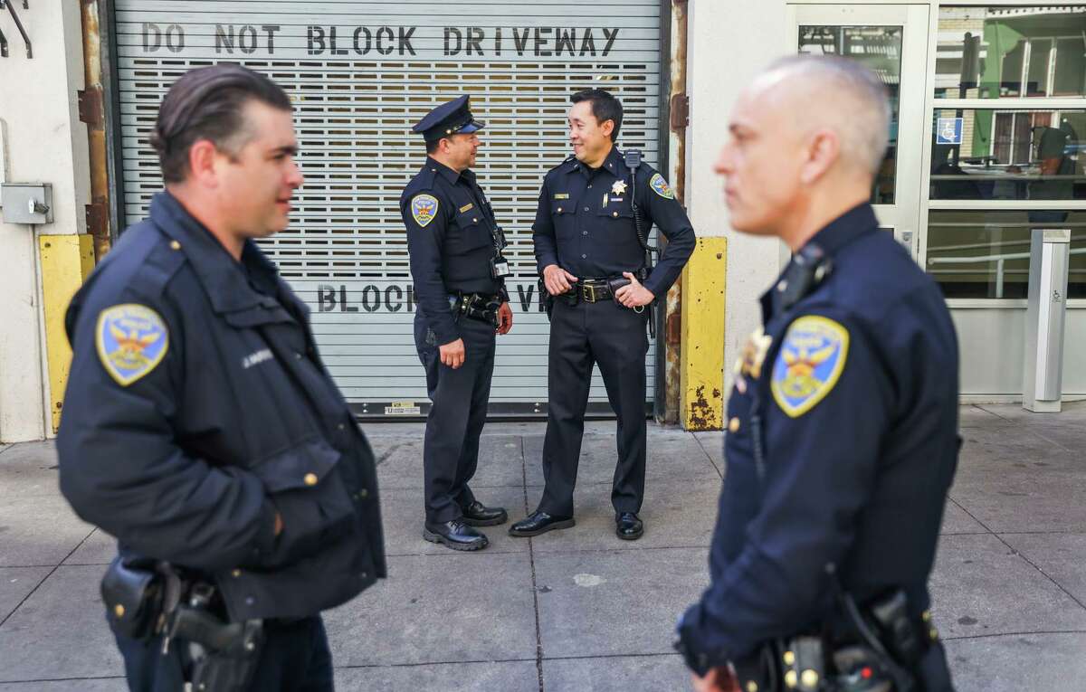 San Francisco Police officer Alberto Duarte (center, left) and Commander Daryl Fong (center, right) chat outside the Tenderloin Police Station on Wednesday, March 16, 2022 in San Francisco, California. The Tenderloin Station got 20 more officers pulled from across the city to help with policing the neighborhood.