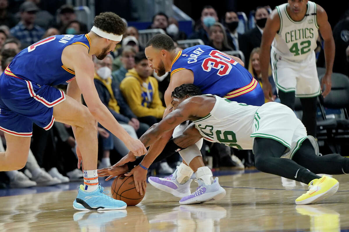 Boston Celtics guard Marcus Smart, bottom, reaches for the ball against Golden State Warriors guard Stephen Curry and guard Klay Thompson, left, during the first half of an NBA basketball game in San Francisco, Wednesday, March 16, 2022. Curry left the game after this play. 