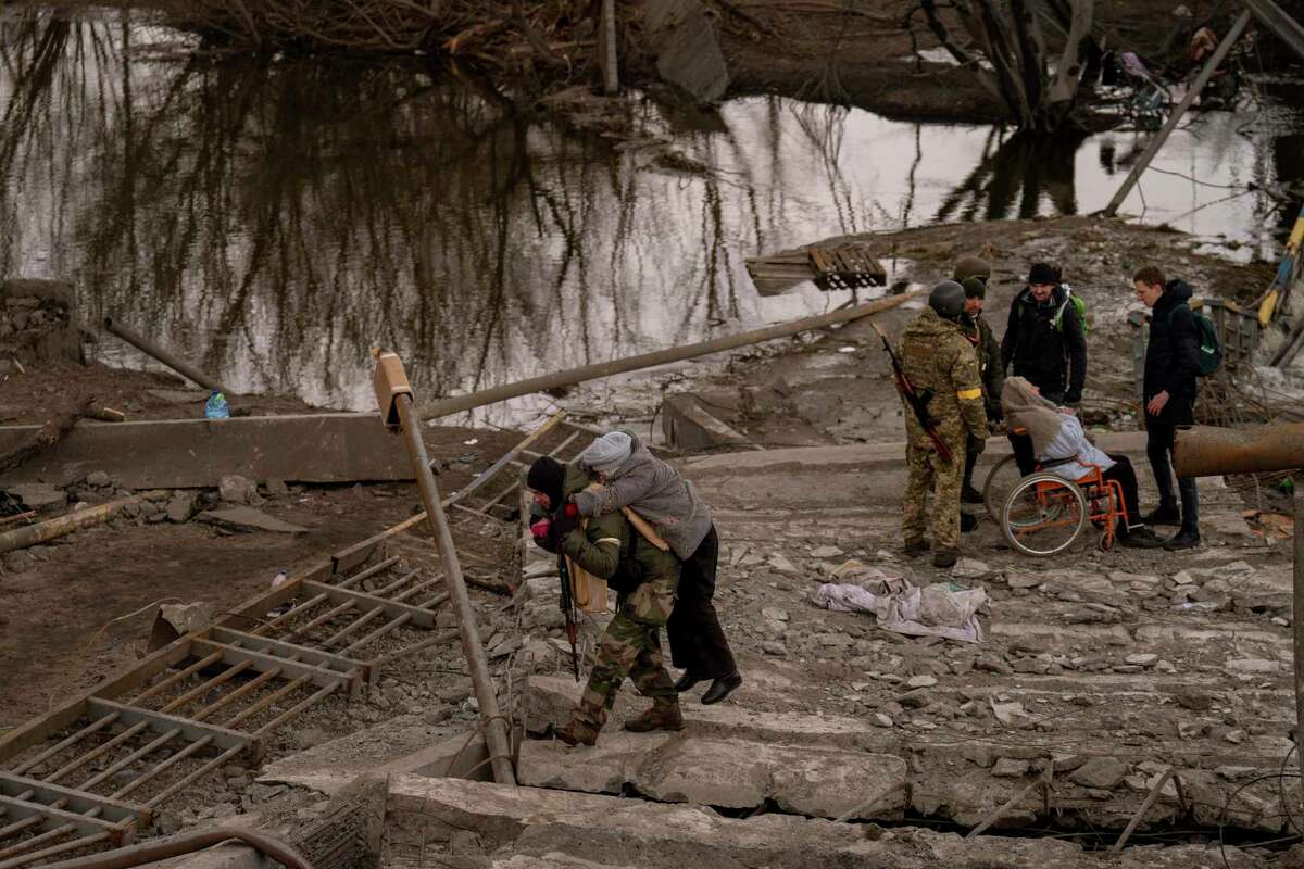 A Ukrainian soldier carries an elderly woman crossing the Irpin river on the outskirts of Kyiv, Ukraine, Monday, March 7, 2022.