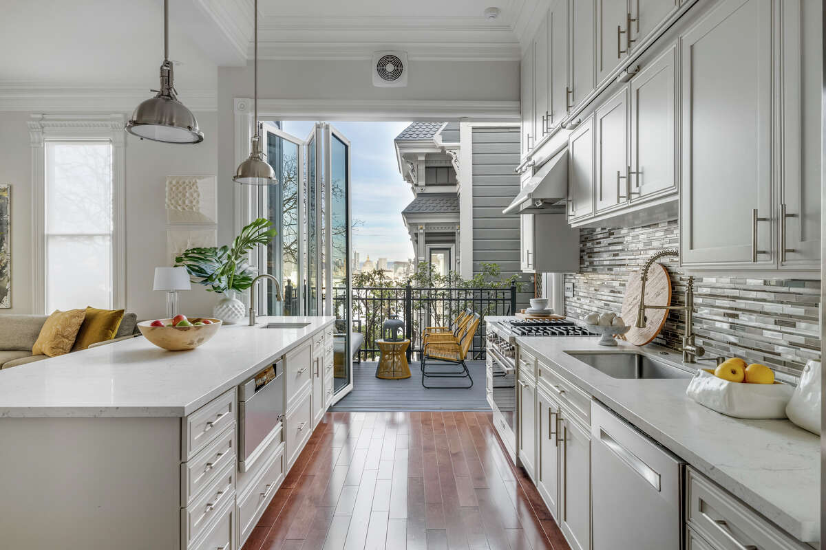 The kitchen is modern and open, featuring folding glass doors that open to a balcony and views.