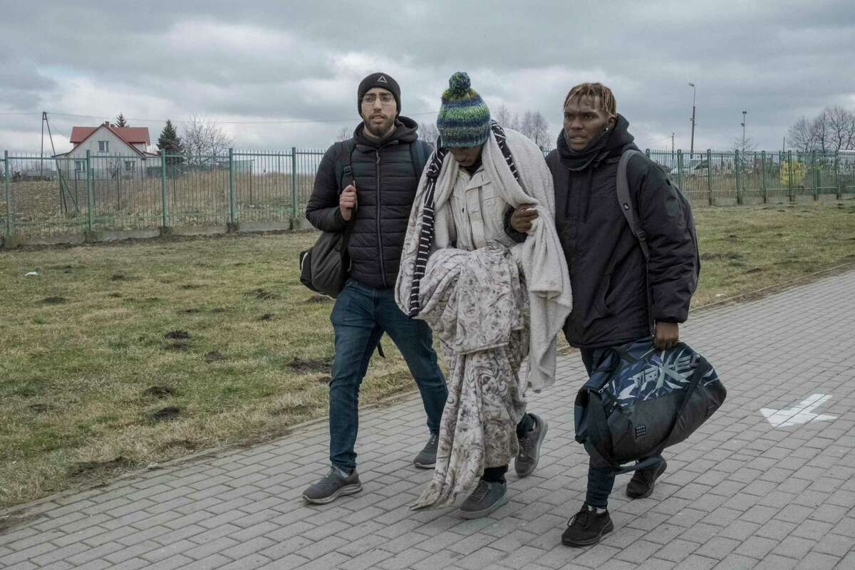 Martin Mpofu, center, a student from Zimbabwe in weak health, is helped by his brother Maneedi, right, and Hatim Redouani, from Morocco, as they cross from Ukraine into in Medyka, Poland, Feb. 28, 2022. Africans who had been living in Ukraine say they were stuck for days at crossings into neighboring European Union countries, held up by Ukrainian authorities who pushed them to the ends of long lines and even beat them, while letting Ukrainians through. (Mauricio Lima/The New York Times)