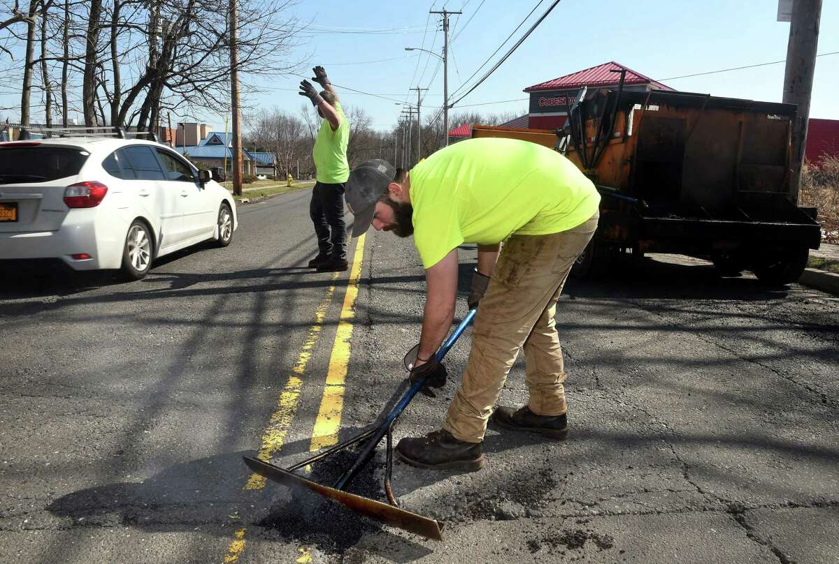 Hamden Public Works crew members John Landino, left, directs traffic while Ron Esposito levels off a filled pothole on Putnam Avenue in Hamden Friday.
