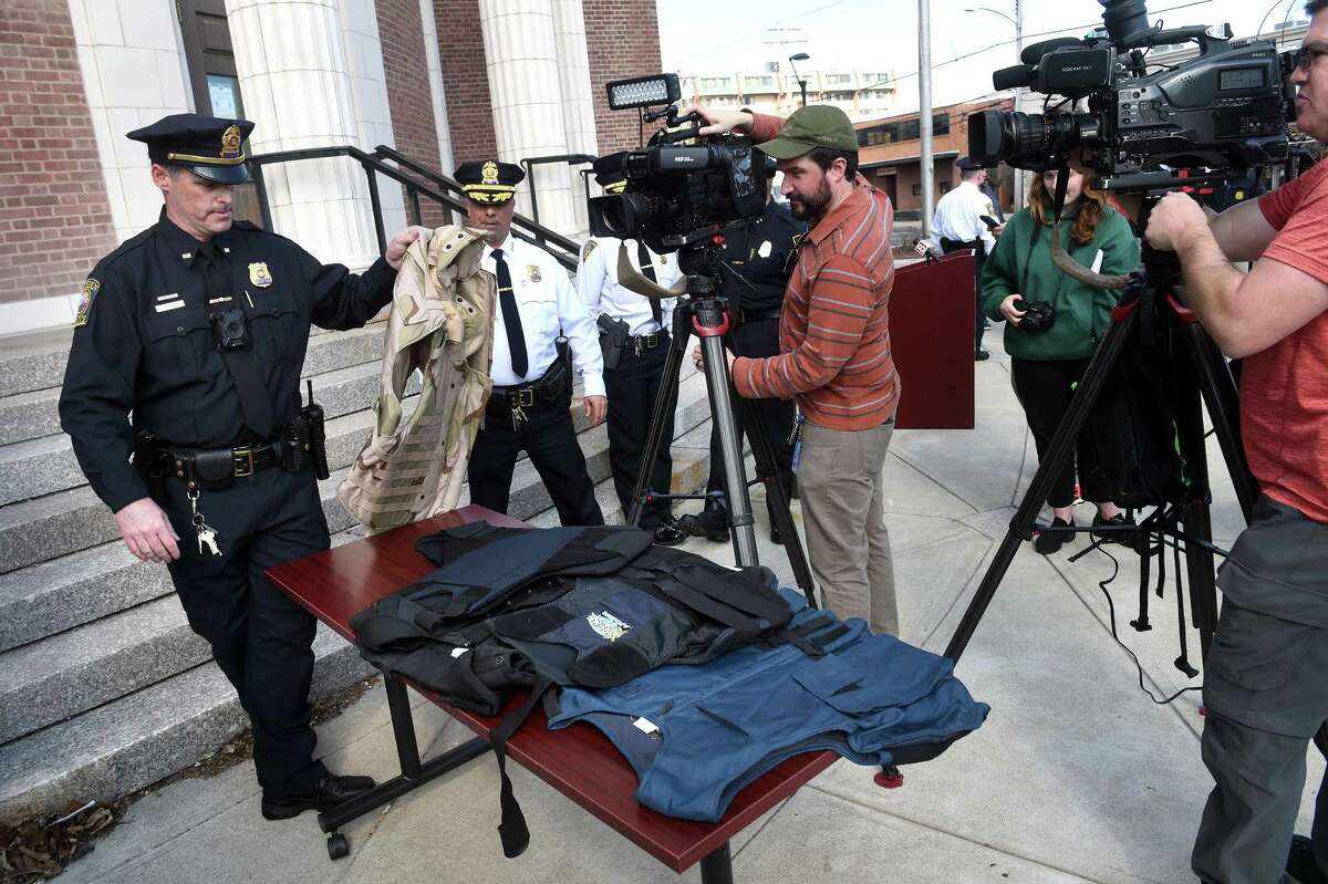 Hamden police Detective Sean Dolan holds one of the ballistic vests headed for Ukraine while television crews prepare to film during a press conference in front of Hamden Memorial Town Hall Friday.