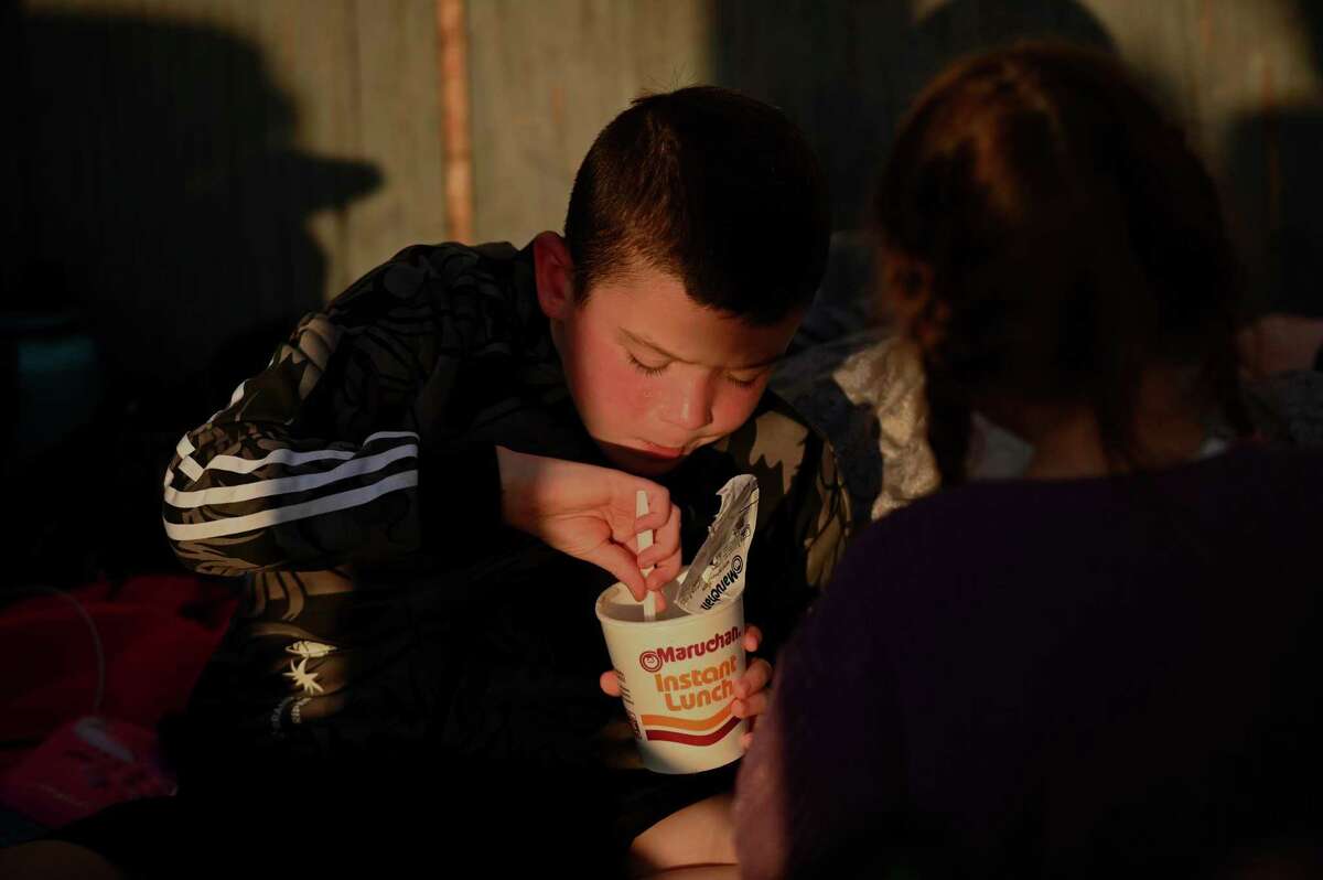 2022年3月16日星期三，一名俄罗斯男孩在蒂华纳的圣伊西德罗入境口岸和家人一起等待时喝着一杯面汤。
