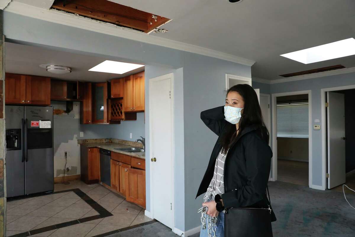 Jennifer Sun stands below two holes in the ceiling of her home, part of the damage from squatters. She and her husband have had to hire private security while they wait for permits to remodel their new home.