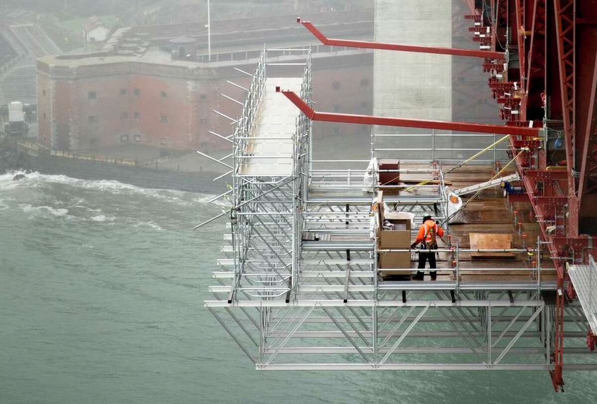 A worker installs large struts for stainless steel netting to flank the Golden Gate Bridge and catch people who jump.