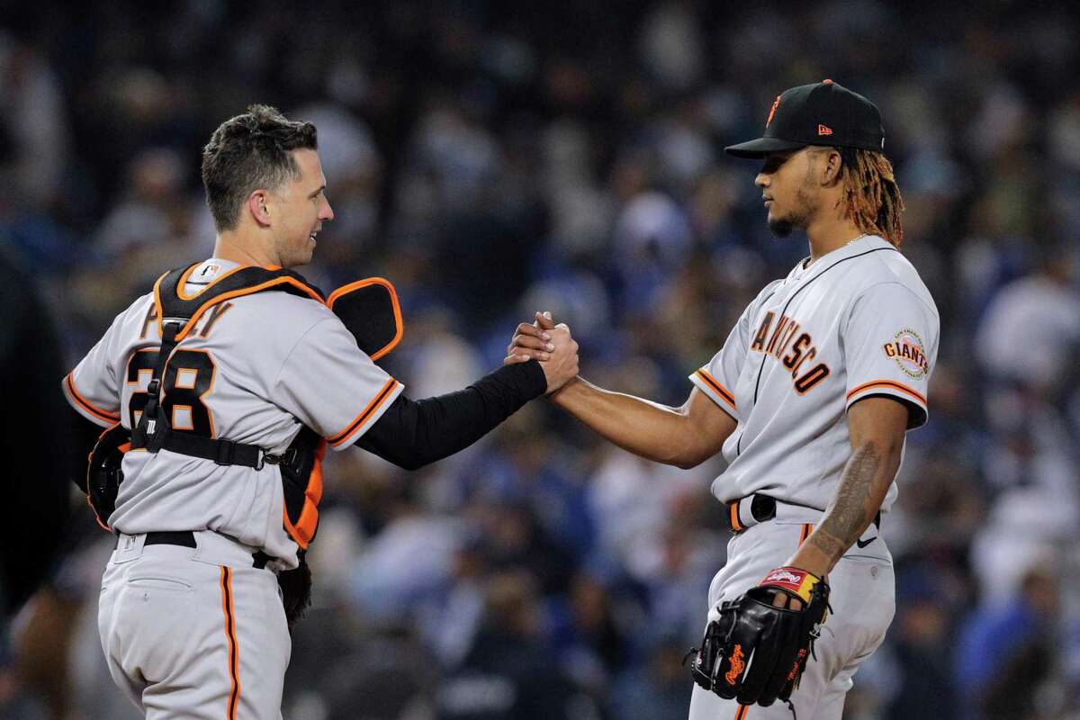 San Francisco Giants Buster Posey (28) shakes hands with closer Camilo Doval (75) after the San Francisco Giants defeated the Los Angeles Dodgers 1-0 in Game 3 of the National League Division Series at Dodger Stadium in Los Angeles, Calif. on Monday, Oct. 11, 2021.