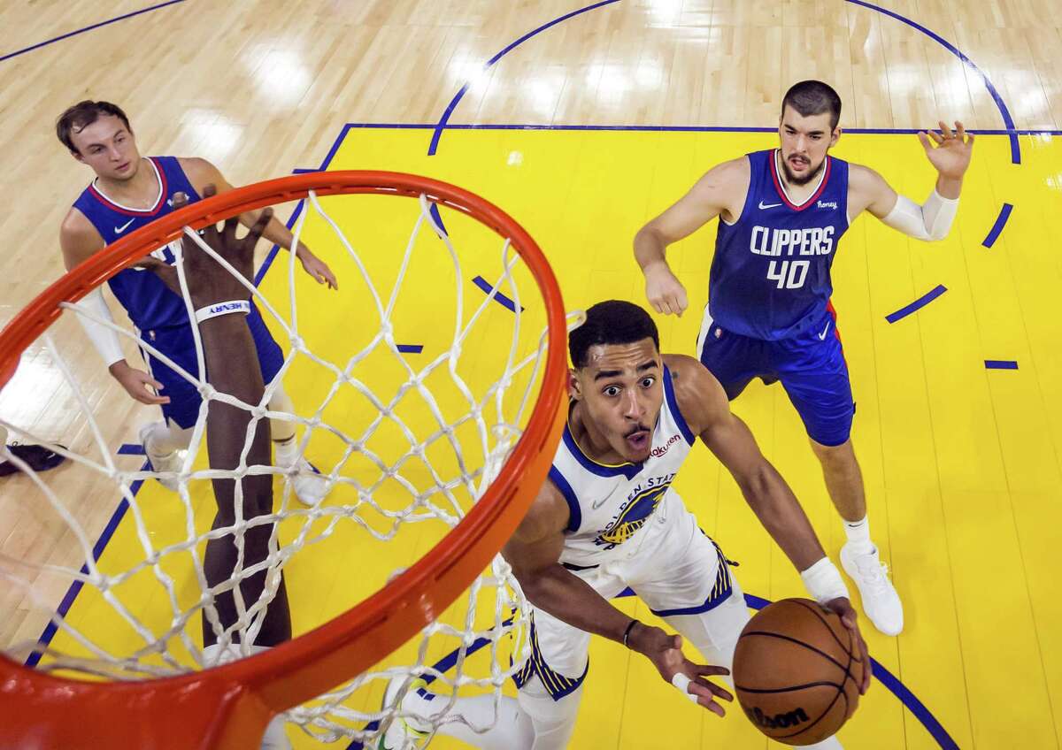 Jordan Poole (3) slips past the defenders for a reverse layup in the second half as the Golden State Warriors played the Los Angeles Clippers at Chase Center in San Francisco, Calif., on Tuesday, March 8, 2022.