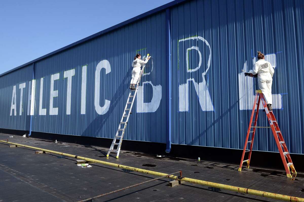 Roxy Prima, left, and Phoebe Cornog from Pandr Design Co., of San Diego, paint a sign on the upper exterior of Athletic Brewing Company’s new brewery in Milford, Conn. March 18, 2022.