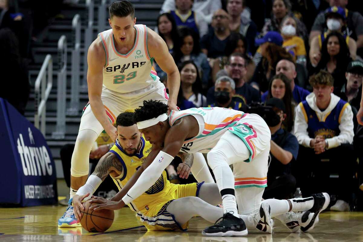 Golden State Warriors guard Chris Chiozza, center, dives for a loose ball against San Antonio Spurs forward Zach Collins, left, and guard Josh Richardson, right, during the first half of an NBA basketball game in San Francisco, Sunday, March 20, 2022. (AP Photo/Jed Jacobsohn)