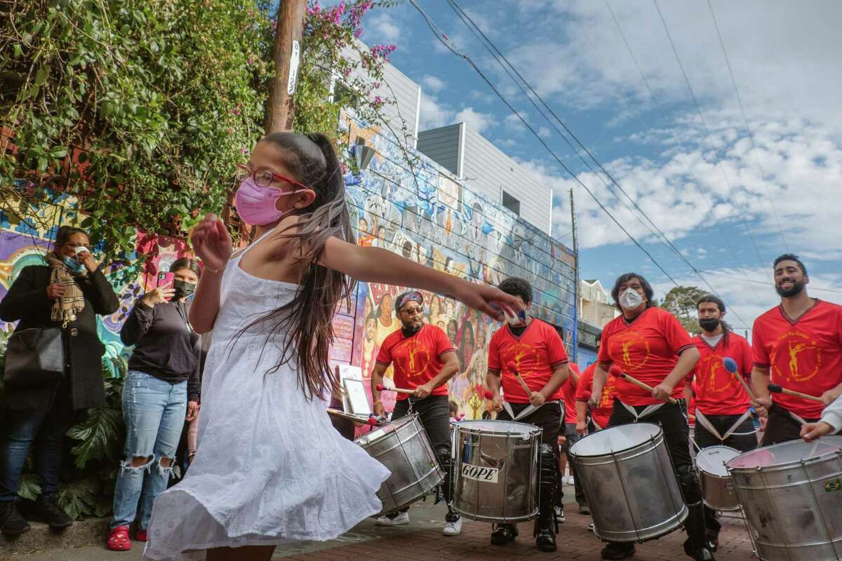 A dancer from the Fogo Na Roupa troupe whirls in front of murals in San Francisco’s Balmy Alley in a recent celebration of female artists and community and business leaders.