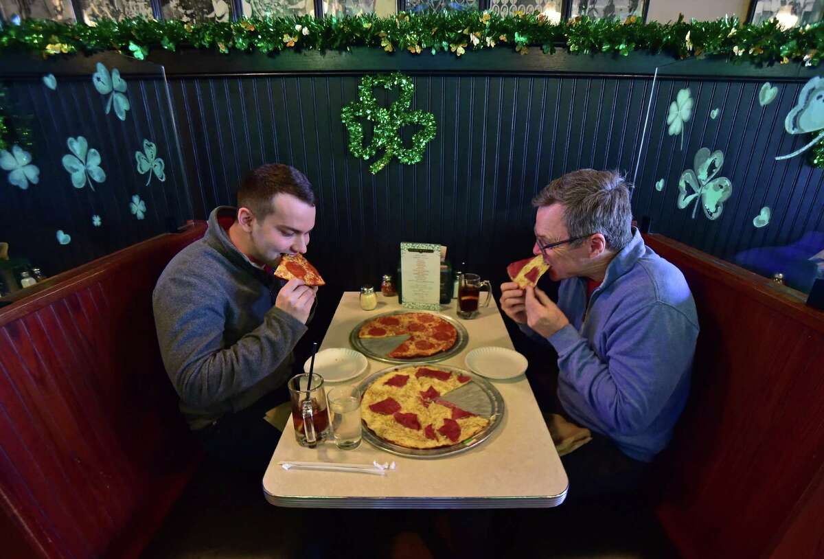 Customers Gib Baltzer, of Stamford, at left, and Joe Stein, of Darien, enjoy pizza at Colony Grill on Myrtle Avenue location in Stamford, Conn., on Friday March 18, 2022. Colony Grill has been a mecca for pizza since 1935 and serves locals at its original location. Colony Grill has expanded over the years, with restaurants now in Florida.
