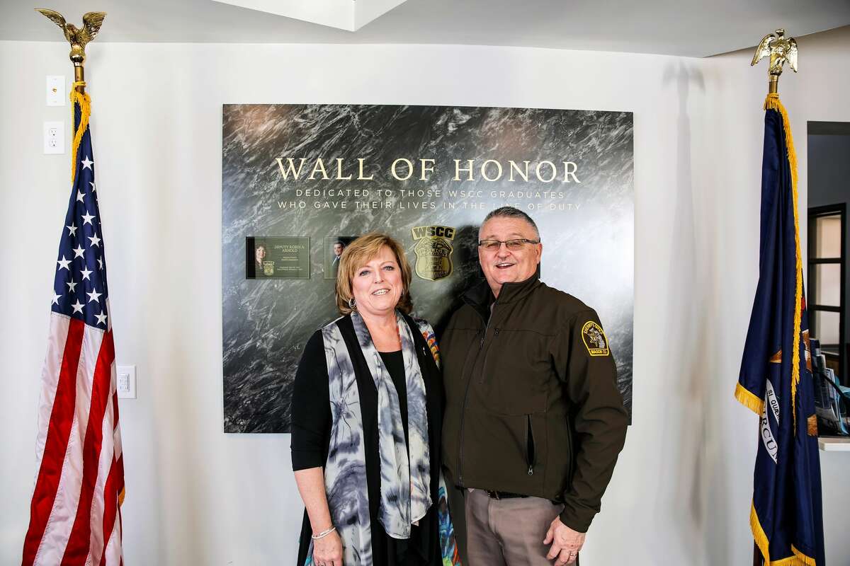 In this file photo, Sherry Wyman (left), chair of the West Shore Community College Board of Trustees, and Mason County Sheriff Kim Cole stand on Jan. 9 in front of the WSCC Wall of Honor, which pays tribute  to fallen law enforcement officers who were graduates of the college.