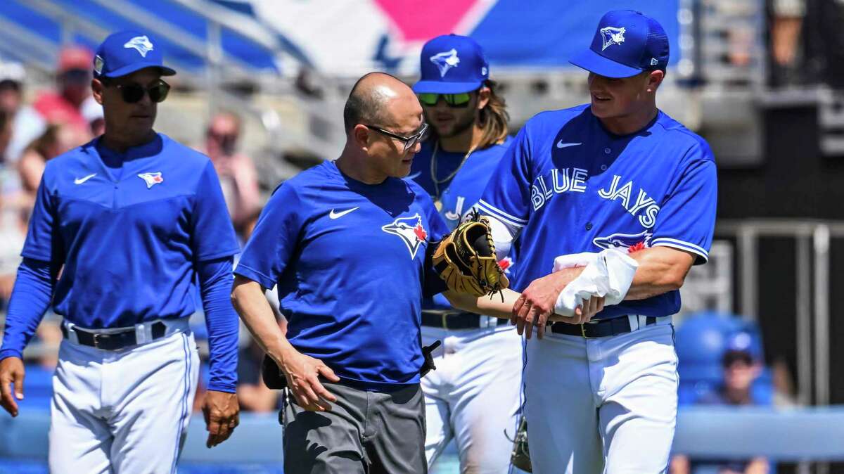 Toronto Blue Jays manager Charlie Montoyo, left, and Bo Bichette look on as Matt Chapman, right, leaves the game with a trainer after suffering an injury tagging out New York Yankees‚'Ender Inciarte at third base during the fourth inning of a spring training baseball game at TD Ballpark Tuesday, March 22, 2022, in Dunedin, Fla. (Steve Nesius/The Canadian Press via AP)