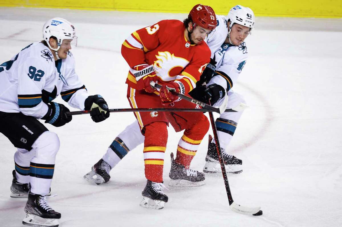 San Jose Sharks' John Leonard, right, steals the puck from Calgary Flames' Johnny Gaudreau, center, as Rudolfs Balcers checks during the first period of an NHL hockey game Tuesday, March 22, 2022, in Calgary, Alberta. (Jeff McIntosh/The Canadian Press via AP)