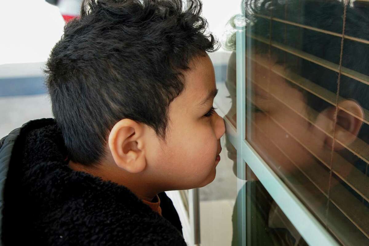 Ezequiel presses his face onto a window as he waits for his mom to get off the phone outside the long-stay hotel they are living in, on Wednesday, March 16, 2022, in Conroe.