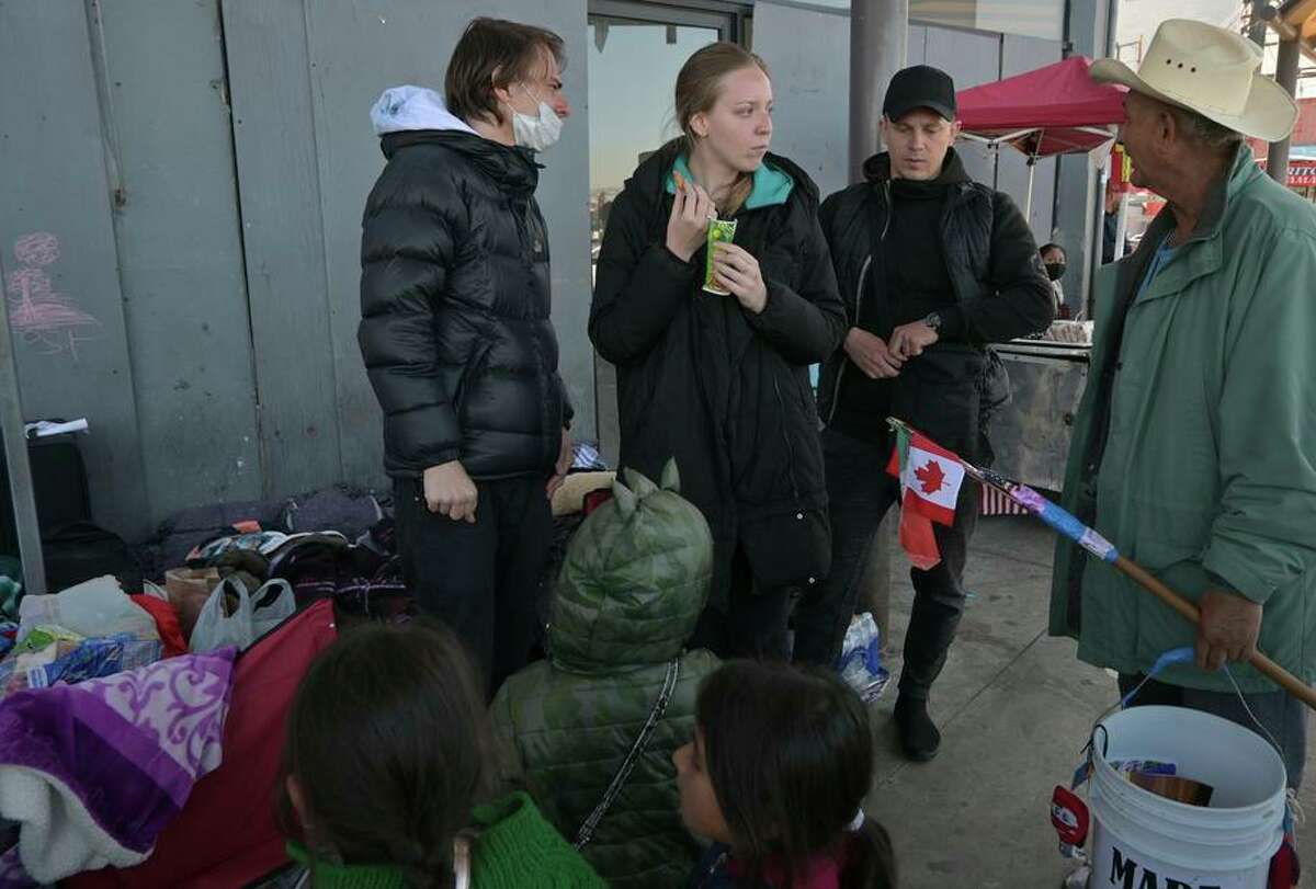 Russian asylum seekers Anton (left) and Julia speak with a street vendor and children from Mexico outside the San Ysidro port of entry in Tijuana this month. Since U.S. Customs and Border Protection took the couple into custody on Sunday, their attorney has only been able to contact them once and does not know where they are.