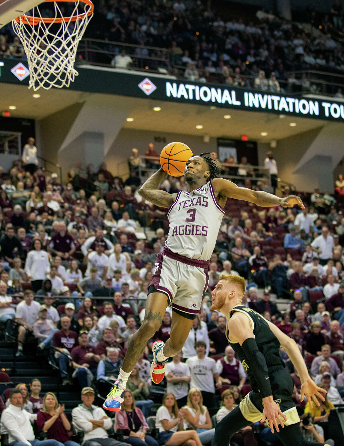 Texas A&M's Quenton Jackson (3) flies through the air for a dunk over Wake Forest's Cameron Hildreth during the first half of an NCAA college basketball game in the third round of the NIT in College Station, Texas, Wednesday, March 23, 2022. (Michael Miller/College Station Eagle via AP)