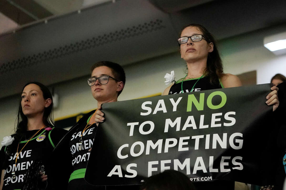 Protesters, one holding a sign, stand as Pennsylvania transgender athlete Lia Thomas competes in the women's 200 freestyle final at the NCAA swimming and diving championships Friday, March 18, 2022, at Georgia Tech in Atlanta. Thomas finished tied for fifth place. 