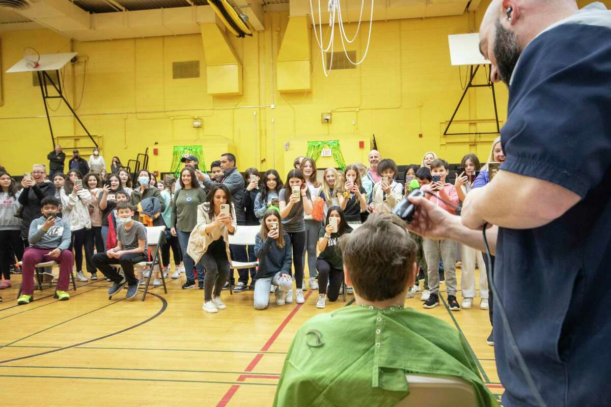 Friends, family and classmates pull out their phones to snap pictures as hair begins to fall to the gymnasium floor during the St. Baldrick’s fundraiser at Western Middle School Thursday, March 24, 2022.