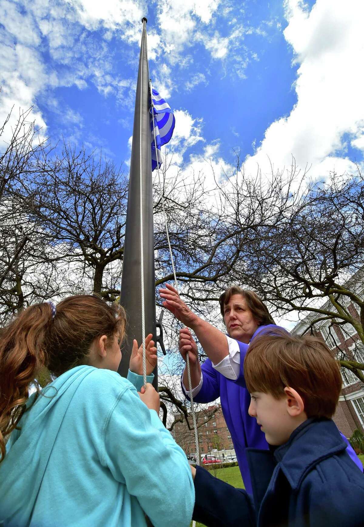 Karen Fassuliotis raises the flag of Greece with some help from Eliana Kassaris, 9, left, and Chris Harmantzis, 5, during a flag raising ceremony to mark Greek Independence Day at Town Hall in Greenwich, Conn., on Friday March 25, 2022.