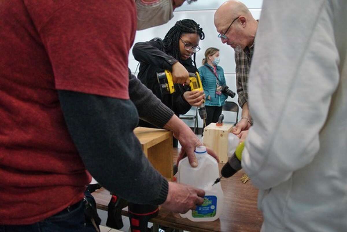 Eighth grader Lashon Fraser, 13, uses a drill as her teacher Larry Drew holds the milk jug at Stephen and Harriet Myers Middle School on Monday, March 7, 2022, in Albany, N.Y. Volunteers with The Vegetable Project were at the school on Monday to show children how to create small greenhouse out of milk jugs.