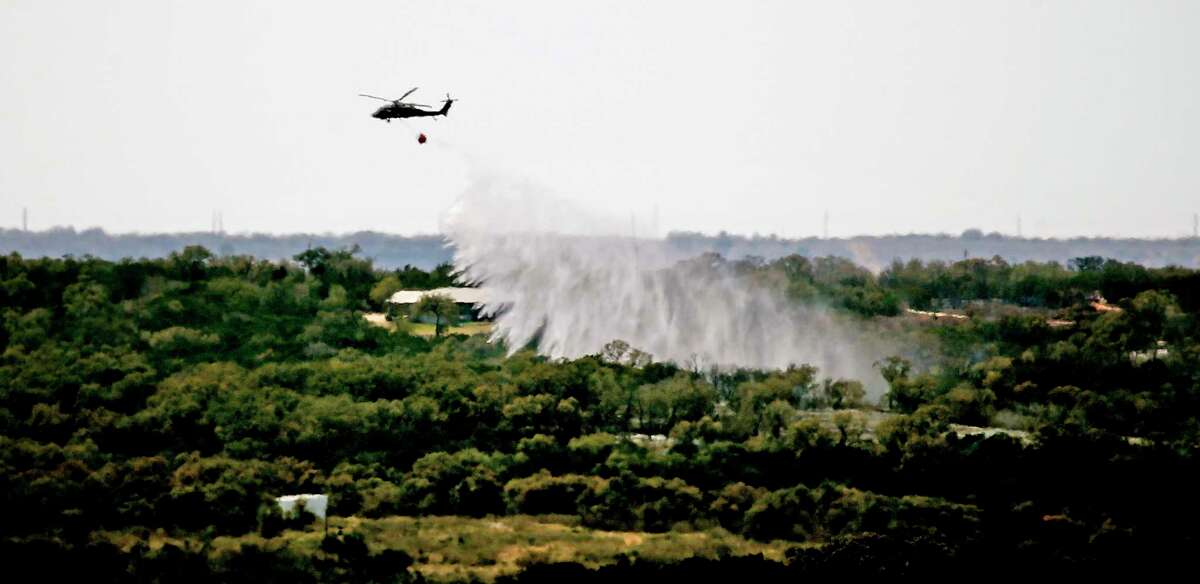 Helicopters pour water on the area south of Medina Lake near the city of Mico on Sunday, March 27. Residents of that lakeside town were ordered to evacuate.