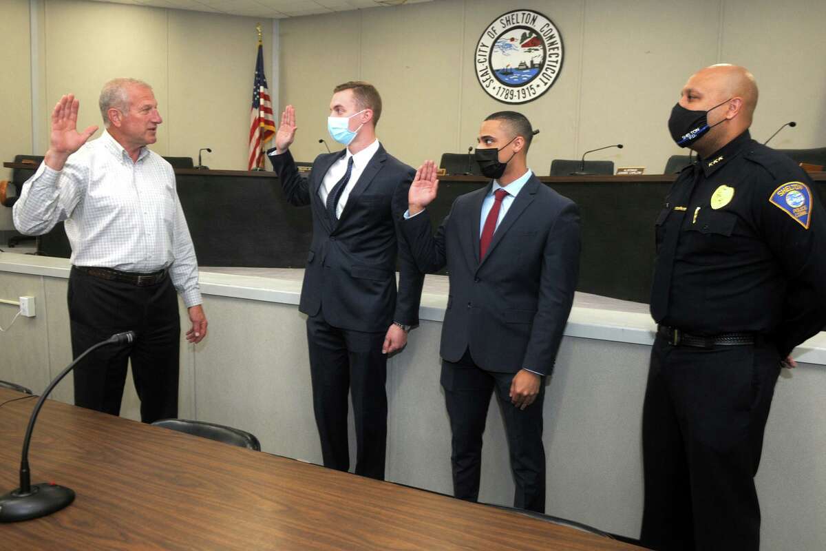 From left, Mayor Mark Lauretti swears in two new recruits to the Shelton Police Department, Steve Kernstock and Lonnie Blackwell, at Shelton City Hall in Shelton, Conn. April 13, 2021. They are seen here with Police Chief Shawn Sequeira, right. The city says it is not having trouble recruiting, although many department across the state are finding it hard to attract qualified candidates.