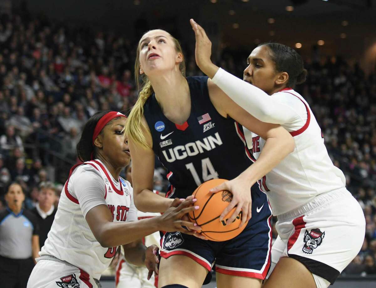 UConn forward Dorka Juhasz, center, powers through NC State defenders Jada Boyd, left, and Camille Hobby on a play in which she was injured in the NCAA women's basketball tournament Elite Eight matchup between No. 2 UConn and No. 1 NC State at Total Mortgage Arena in Bridgeport, Conn. Monday, March 28, 2022.