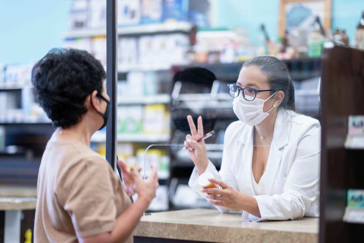 A woman talks to her pharmacist about her medication being picked up at a pharmacy. 