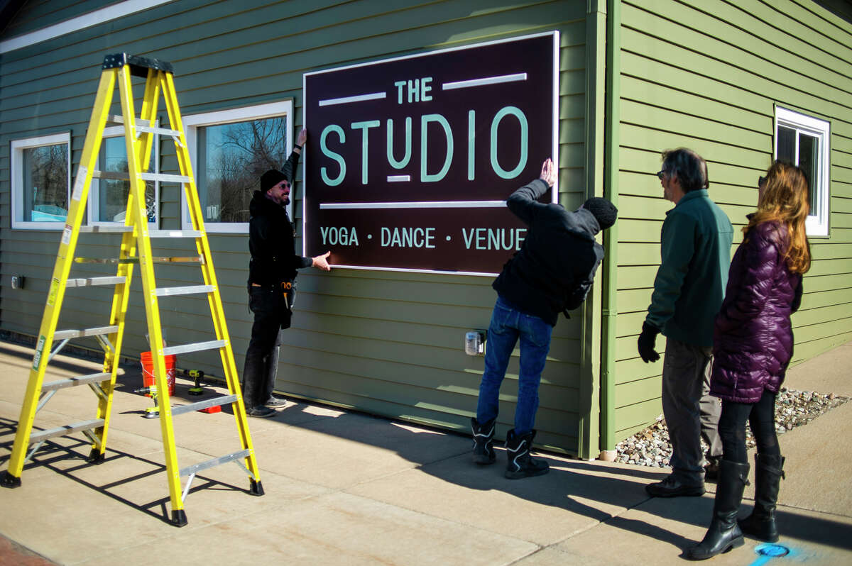 Debbie Bacus, far right, and Lon Wackerle, second from right, watch as Avram Golden, left, and Nick VanHorn, center, of Golden Gallery and Custom Framing prepare to hang a brand new sign outside of The Studio, located at 328 W. Saginaw Road in downtown Sanford, Tuesday, March 29, 2022.