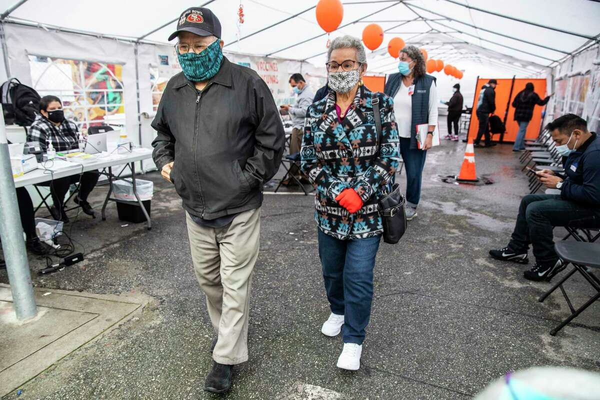 Rueben Arellano, 90, left, and Victoria Jane Arellano, 85, exit a tent after receiving COVID-19 boosters at a community testing and vaccination site managed by Unidos En Salud in the Mission District of San Francisco, California Friday, Jan. 7, 2022.