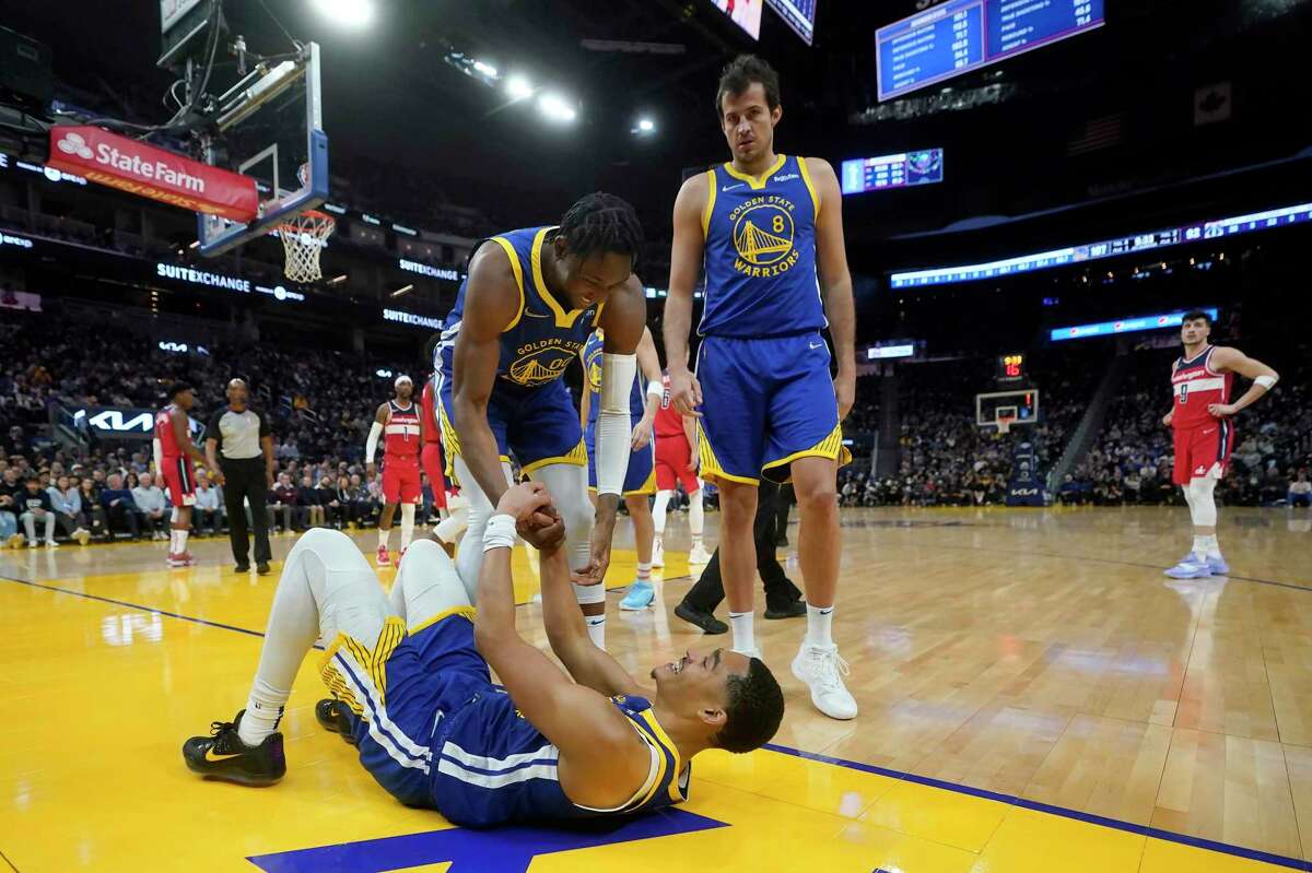Golden State Warriors guard Jordan Poole, bottom, is helped off the floor by forward Jonathan Kuminga as forward Nemanja Bjelica (8) looks on during an NBA basketball game against the Washington Wizards in San Francisco, Monday, March 14, 2022. (AP Photo/Jeff Chiu)