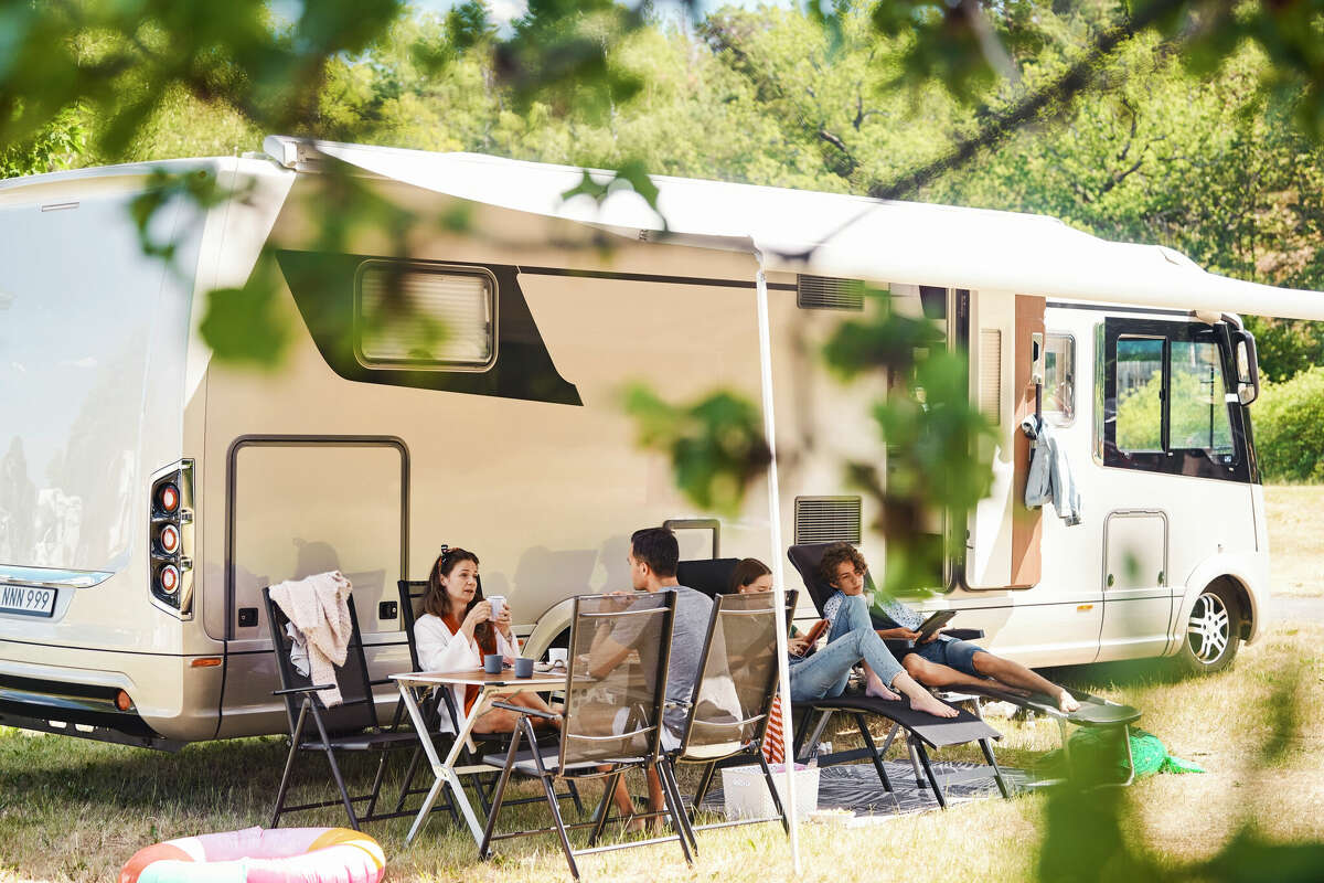 A family relaxes on chairs next to an RV at a campsite.