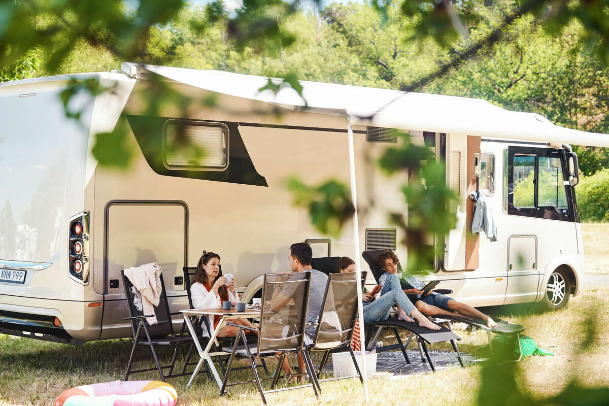 A family relaxes on chairs next to an RV at a campsite. 